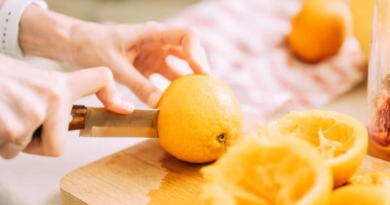 Female expertly slicing a fresh orange in half on a wooden cutting board, demonstrating proper technique for preparing nutrient-rich citrus fruits.