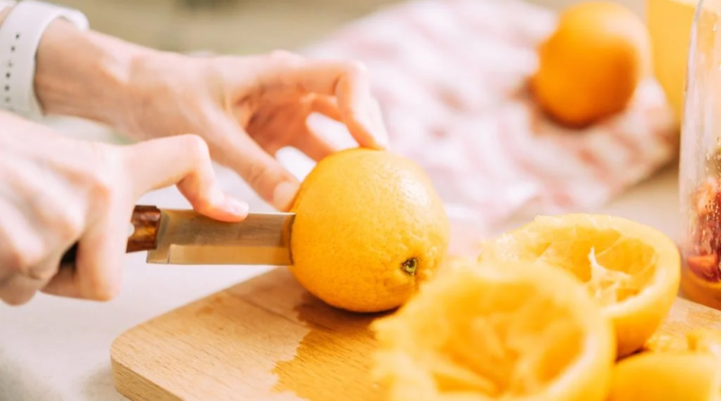 Female expertly slicing a fresh orange in half on a wooden cutting board, demonstrating proper technique for preparing nutrient-rich citrus fruits.