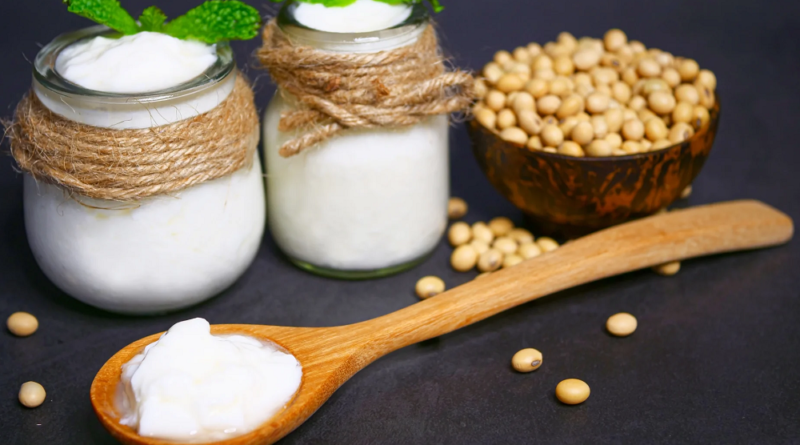 Soy yogurt in a glass jar with a spoon, next to soybeans, representing the natural, plant-based ingredients in soy yogurt.