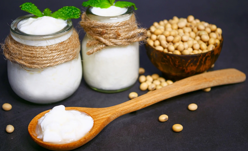 Soy yogurt in a glass jar with a spoon, next to soybeans, representing the natural, plant-based ingredients in soy yogurt.